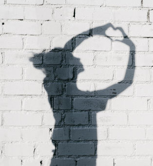 Portrait of a young woman showing a Heart with Her Hands around on the brick wall background. Photo of shadows of girl